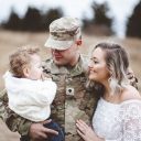 . A young family portrait - a soldier father holding his son and a beautiful young wife wearing a white dress